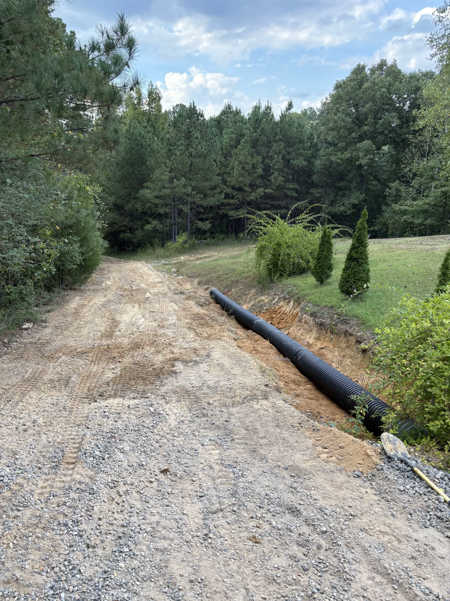 Corrugated drainage pipe installed beside a gravel driveway before final gravel placement